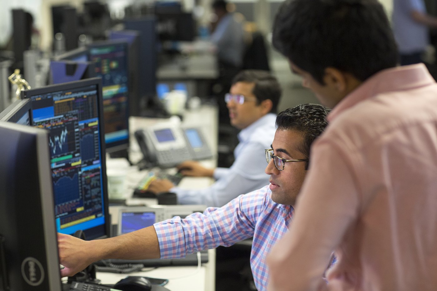 Two colleagues looking at charts shown on desktop monitors on the trading floor.